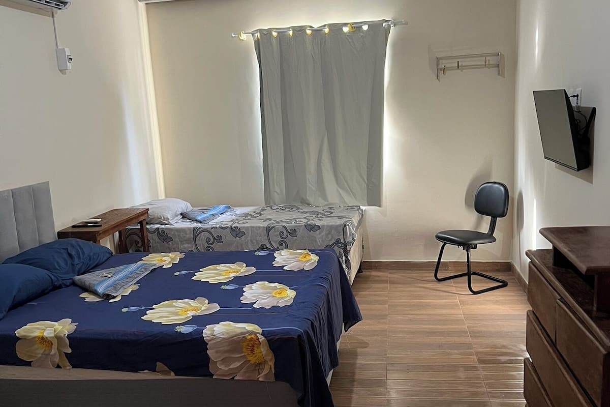 Una camera da letto con due letti, una scrivania, una sedia, un comò e un televisore a parete.
