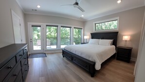 Une chambre dotée d’un grand lit, d’un ventilateur de plafond et offrant une vue sur l’extérieur grâce à de grandes fenêtres.