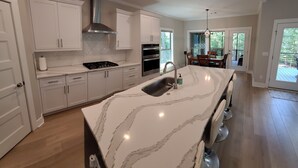 Une cuisine moderne avec des meubles blancs, un îlot en marbre, des appareils électroménagers en acier inoxydable et un coin repas offrant une vue agréable.
