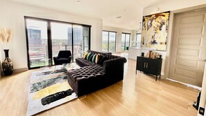 A modern living room with a black sofa, a glass coffee table, and a city view through large windows. - Ceiling to floor windows featuring a private balcony with stunning city views! 
 (Atlanta)