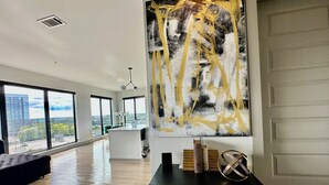 A spacious living area with large windows, a modern black console table, and a large abstract painting. - Ceiling to floor windows featuring a private balcony with stunning city views! 
 (Atlanta)