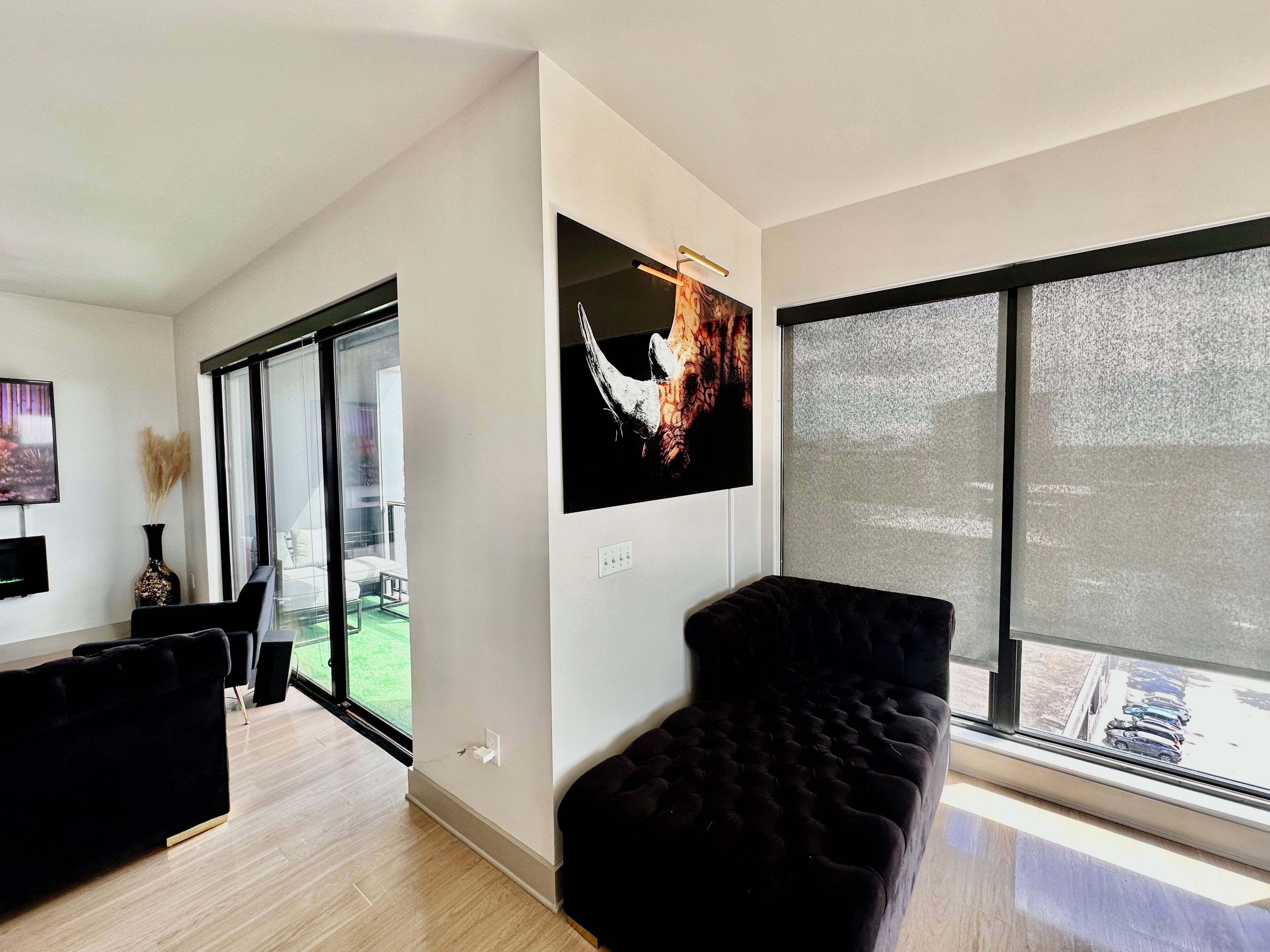 A modern living room with a large window, a black sofa, and a flat-screen TV mounted on the wall.