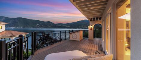 A balcony with a bed, a view of the sea, and a mountainous landscape.