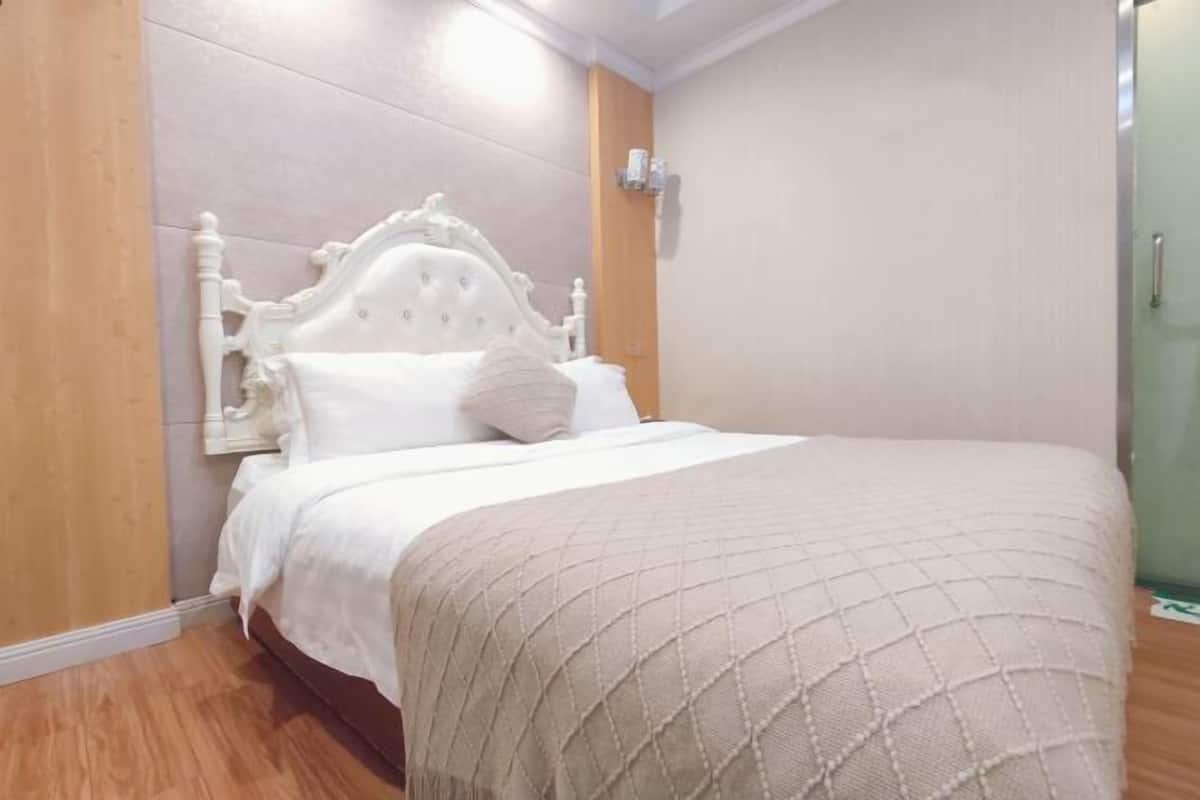 Una cama con cabecera, una mesita de noche y una lámpara de pared.