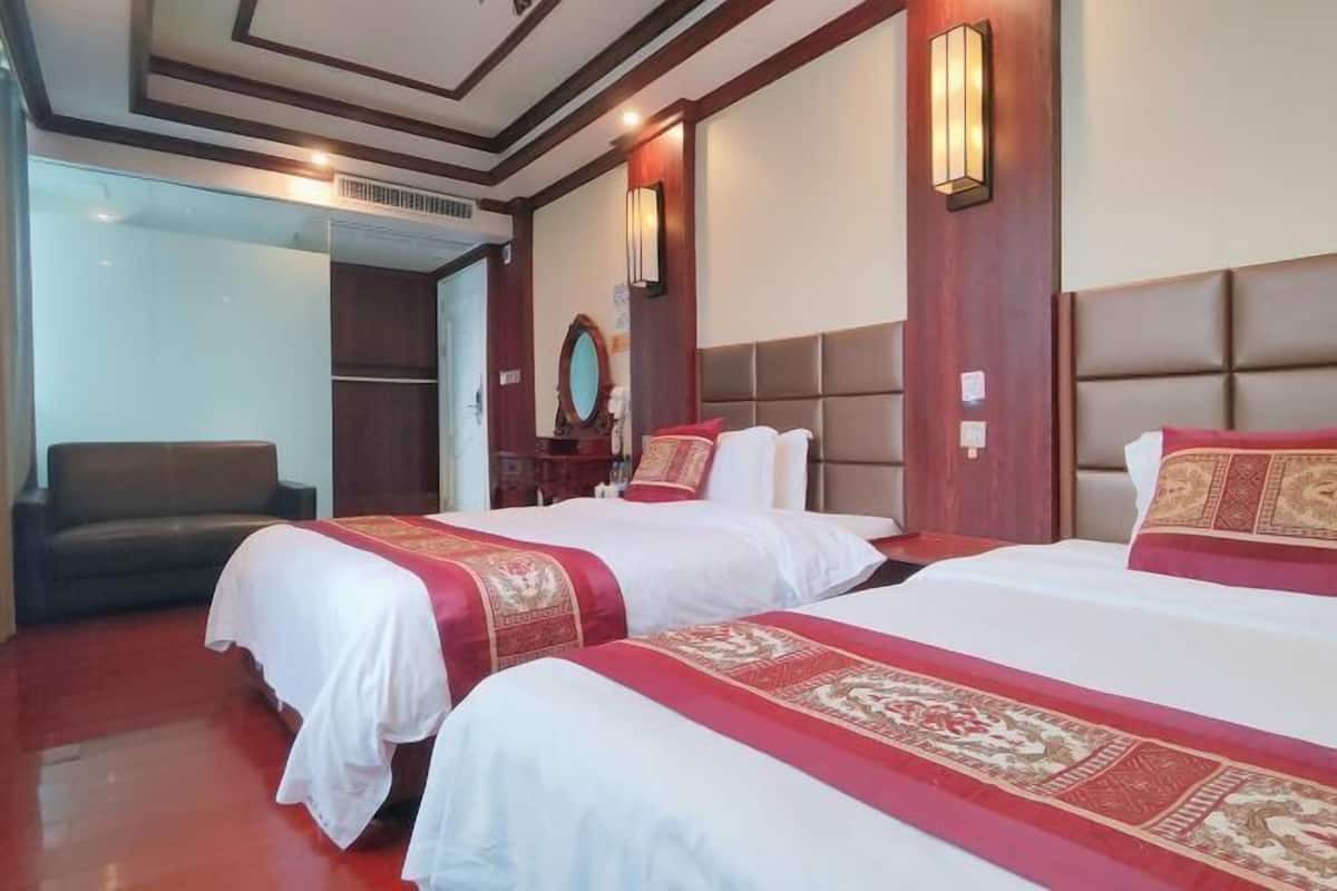 Una habitación de hotel con dos camas, un sofá, un espejo y un cabecero de madera.