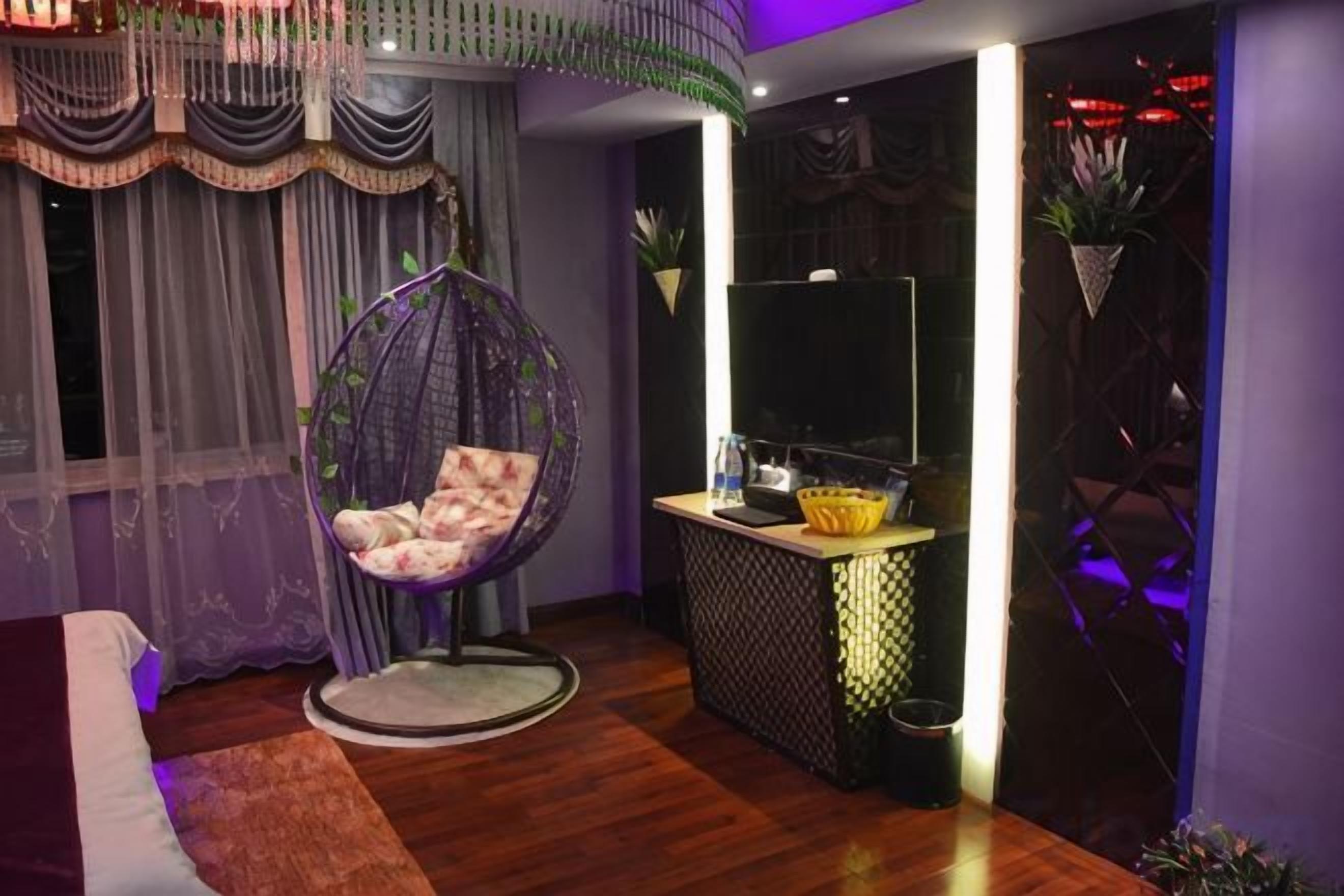 A room with a hanging chair, a flat-screen TV, a small table, and a decorative wall.
