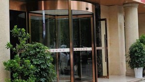 Ein Hotel Eingang mit einer Drehtür, Zimmerpflanzen und einem Schild darüber.