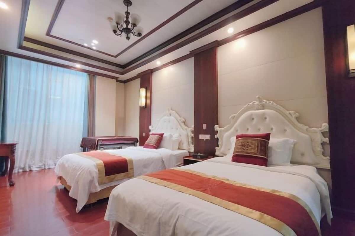 Habitación de hotel con dos camas, una araña y un ventanal con cortinas.