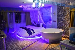 Een slaapkamer met een groot bed, een badkuip en een kroonluchter.