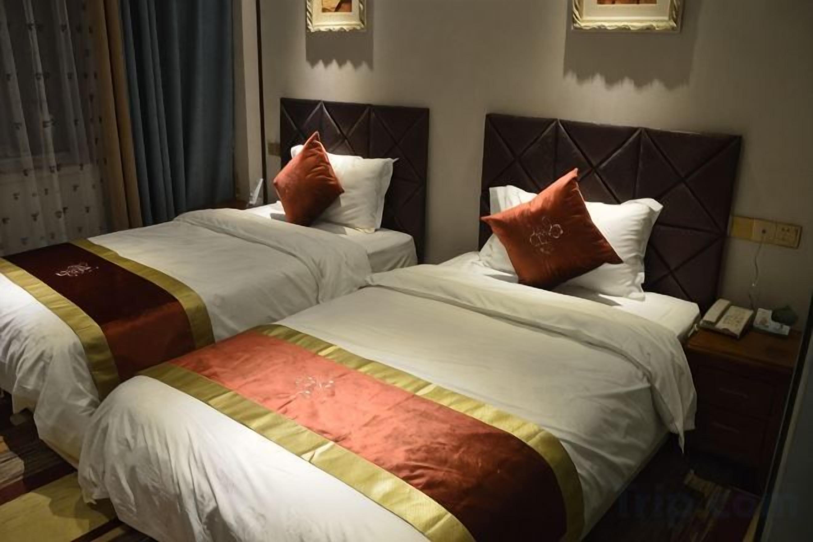 A hotel room with two beds, each with a headboard, a bedside table with a phone, and a curtain on the window.