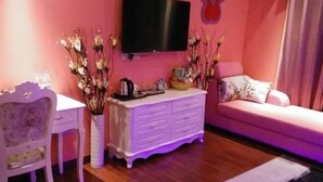 Ein Wohnzimmer mit einem weißen Sofa, einer weißen Kommode, einem an der Wand montierten Fernseher und einer Blumenvase auf der Kommode.