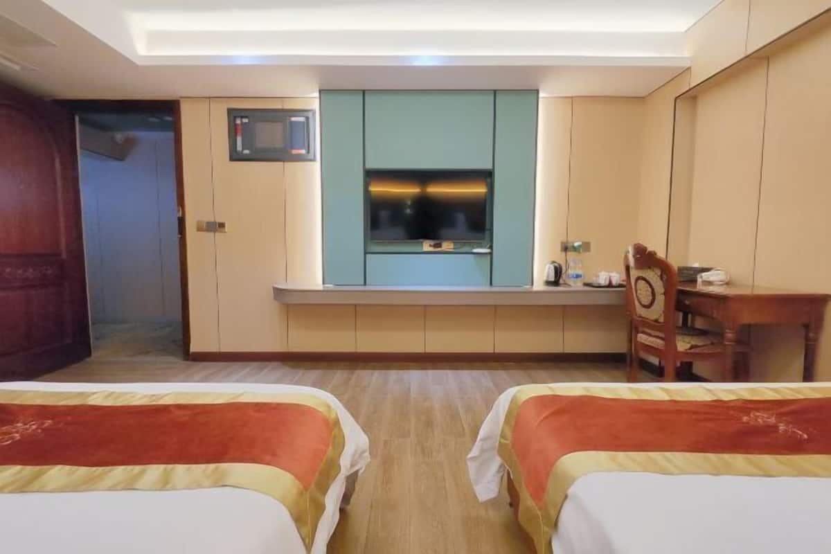 Habitación de hotel con dos camas, un escritorio, un televisor y una nevera pequeña.