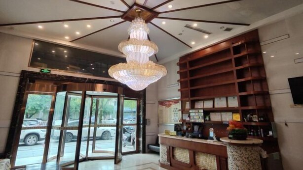 Eine Hotelhalle mit einem Chandelier, Holzregalen, einem Empfangstresen und einem großen Fenster.