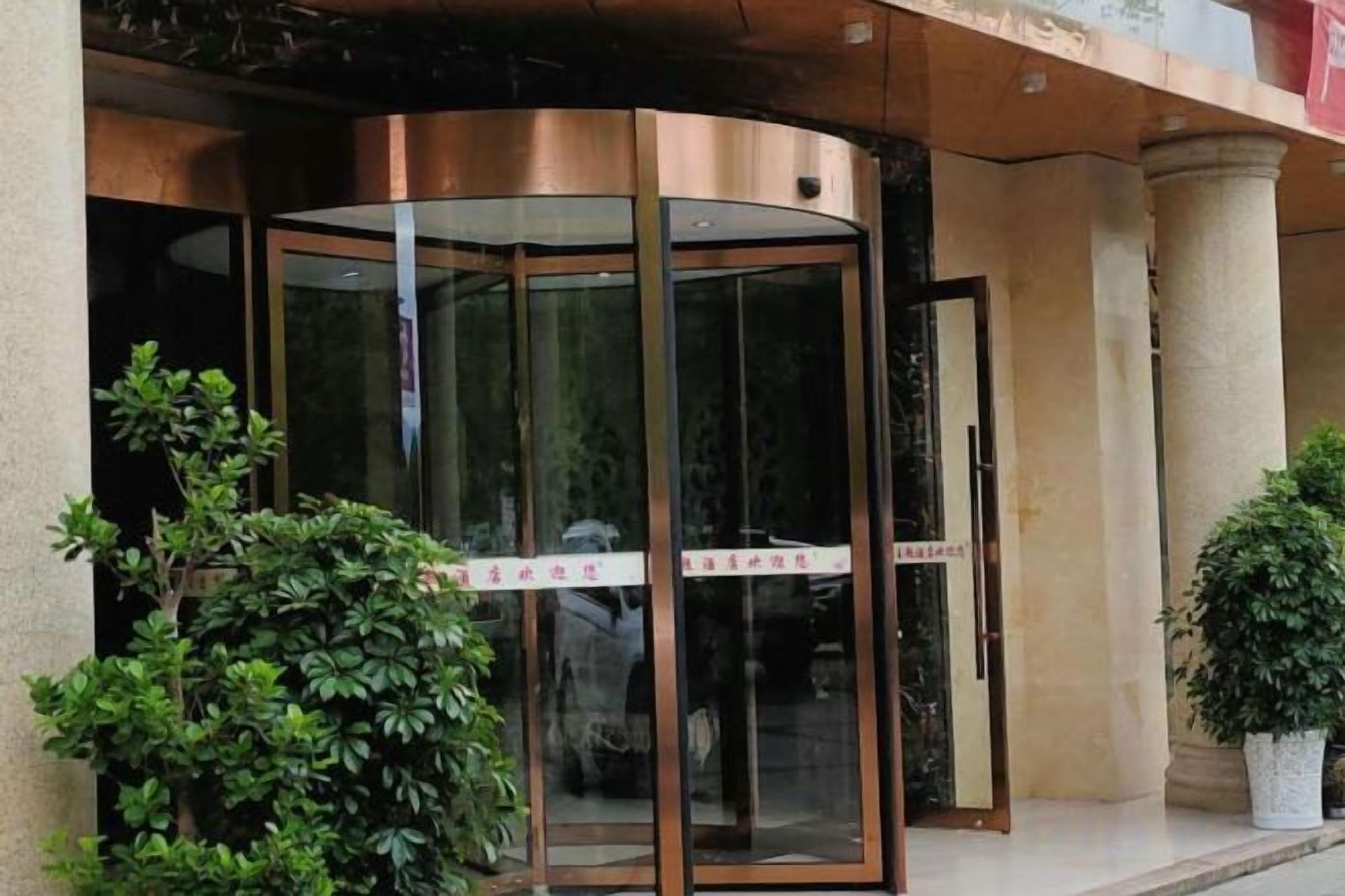 A revolving door entrance with glass panels and a metal frame, flanked by potted plants.