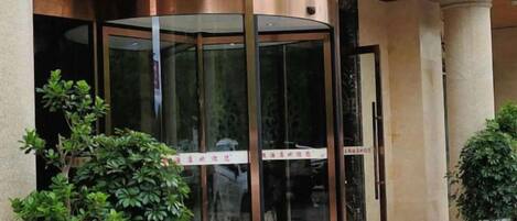 A revolving door entrance with glass panels and a metal frame, flanked by potted plants.