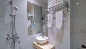 Ein Badezimmer mit einer gläsernen Duschkabine, einem weißen Waschbecken, einem Spiegel und einem Handtuchhalter mit gefalteten Handtüchern.