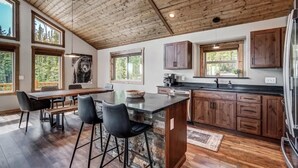 Una cocina moderna con armarios de madera, una isla grande con taburetes de bar y amplios ventanales con vistas al exterior.