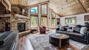Un salón espacioso con chimenea de piedra, ventanas amplias, ventilador de techo y una zona de estar acogedora.