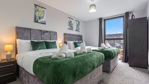 A modern hotel room with two beds, green bedding, a large window, and artwork on the walls. - King Bed | 2bath | Parking | Netflix | City Centre (Birmingham)