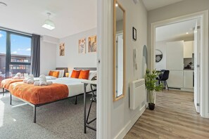 A modern hotel room with a bed, a large window, a view of the city, a dining area, and a potted plant.
