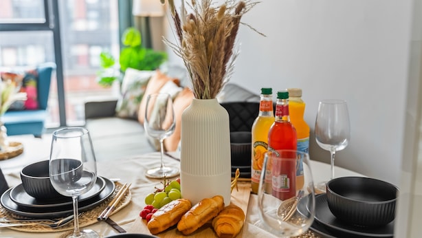A dining table set with plates, glasses, a vase with dried plants, and food items. - King Bed | 2bath | Parking | Netflix | City Centre (Birmingham)