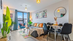 A modern living room with a sofa, dining table, and chairs. There are plants, a mirror, and artwork on the walls. - King Bed | 2bath | Parking | Netflix | City Centre (Birmingham)