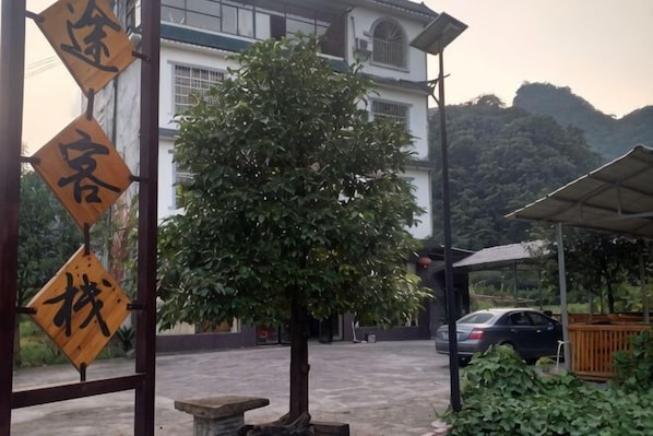 A building with a large tree in front, a covered area, and a parked car.