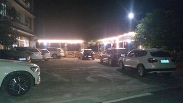 Un estacionamiento con varios autos, un edificio con señalización iluminada y una farola.
