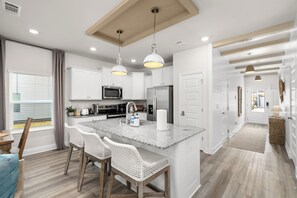 A modern kitchen with white cabinetry, a central island with bar stools, and pendant lighting. - Walk 2 Beach, Stylish 3BR in PCB, Grill (Panama City Beach)