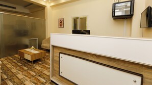 Un'area reception con un tavolino in legno, una scrivania bianca per l'accoglienza, una televisione a parete e un quadro incorniciato.