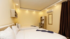 Una camera d'albergo con due letti, un armadio, un condizionatore d'aria e uno specchio.