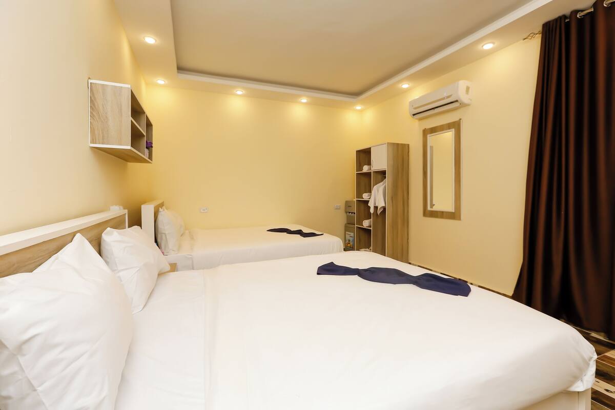 A hotel room with two beds, a wardrobe, an air conditioning unit, and a mirror.