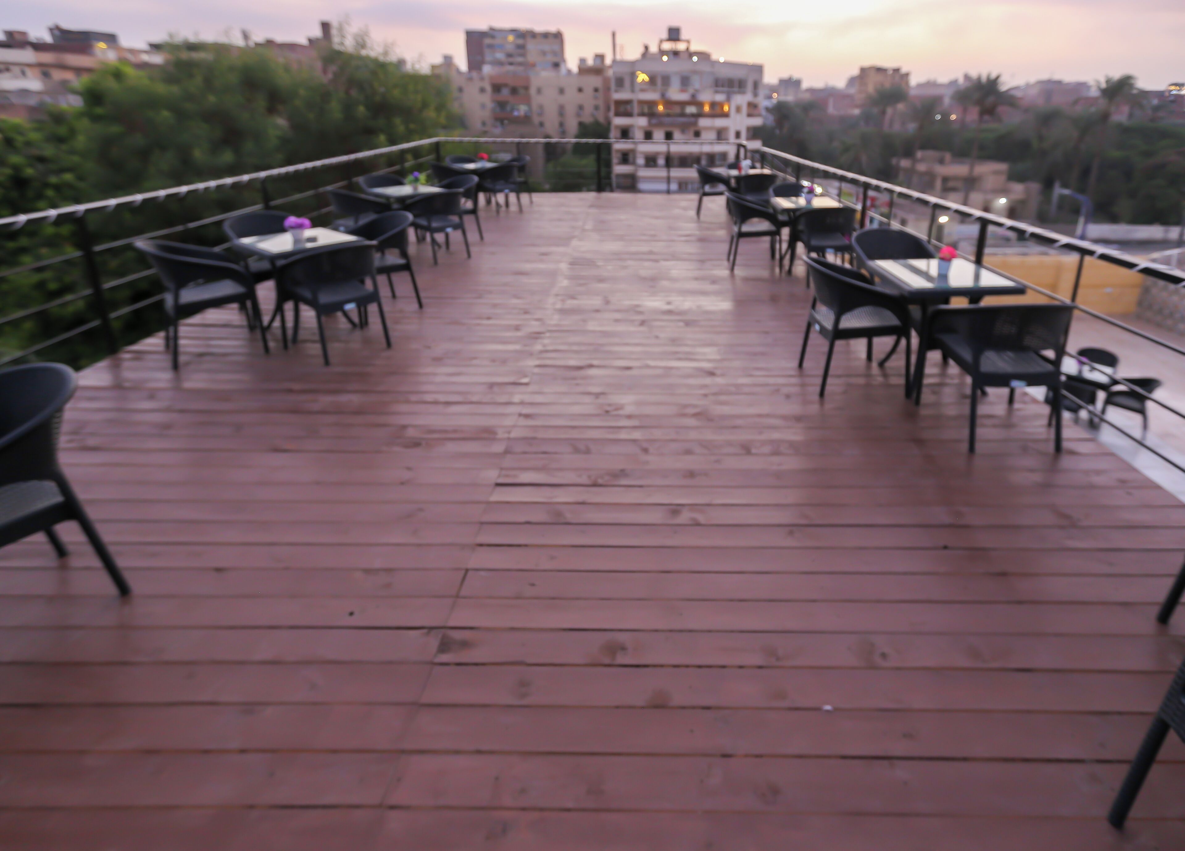 A wooden deck with outdoor seating, including tables and chairs, overlooking a cityscape.