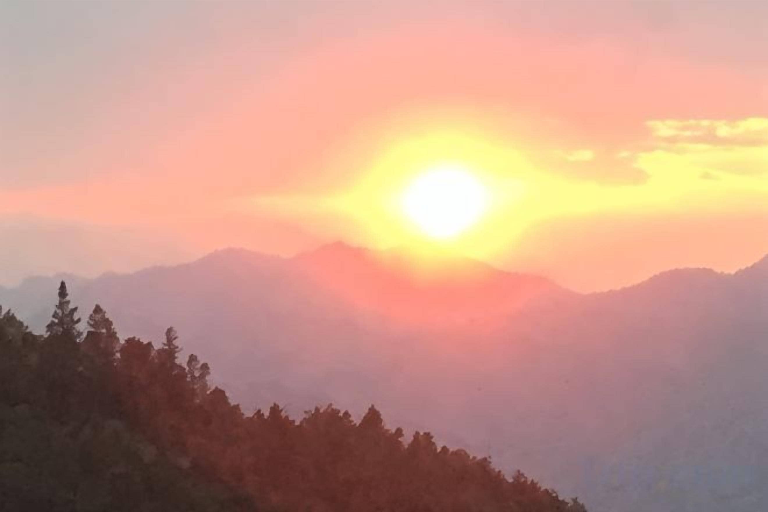 A mountain landscape with a sun setting behind the peaks.