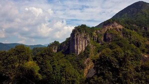 A mountainous landscape with dense forestation and a prominent rock formation.