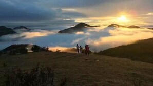 A group of people standing on a grassy hill with a sunset in the background.