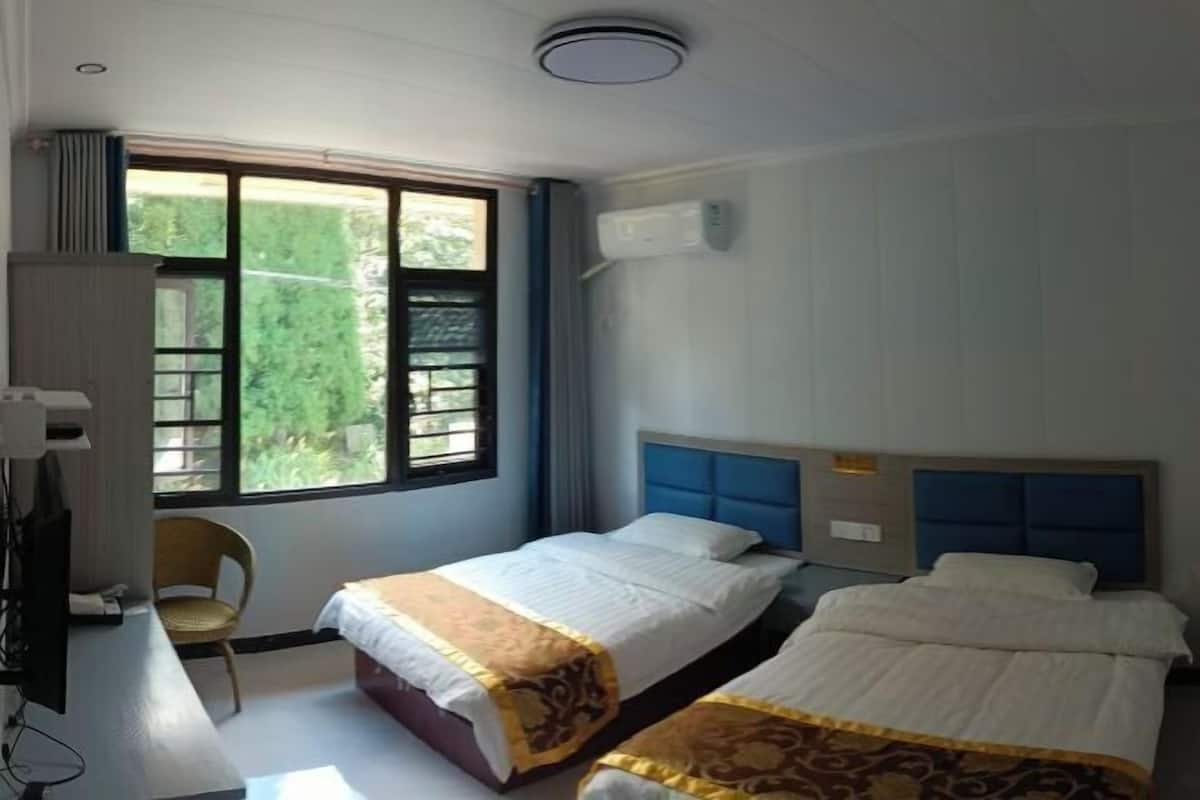 Hotellihuone, jossa on kaksi sänkyä, työpöytä, tuoli ja ikkuna, josta on näkymä vehreään maisemaan.