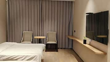 A hotel room with a bed, two chairs, a small round table, a mirror, and a shelf with a plant.