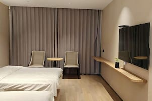 Habitación de hotel con cama, dos sillas, una mesita redonda, espejo y repisa con una planta.