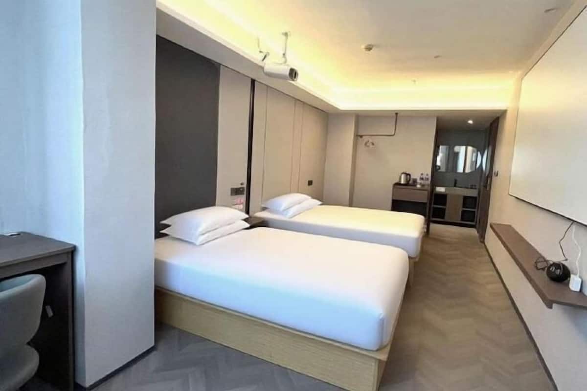 Ein Hotelzimmer mit zwei Betten, einem Schreibtisch, einer Küchenzeile und einem großen Spiegel.