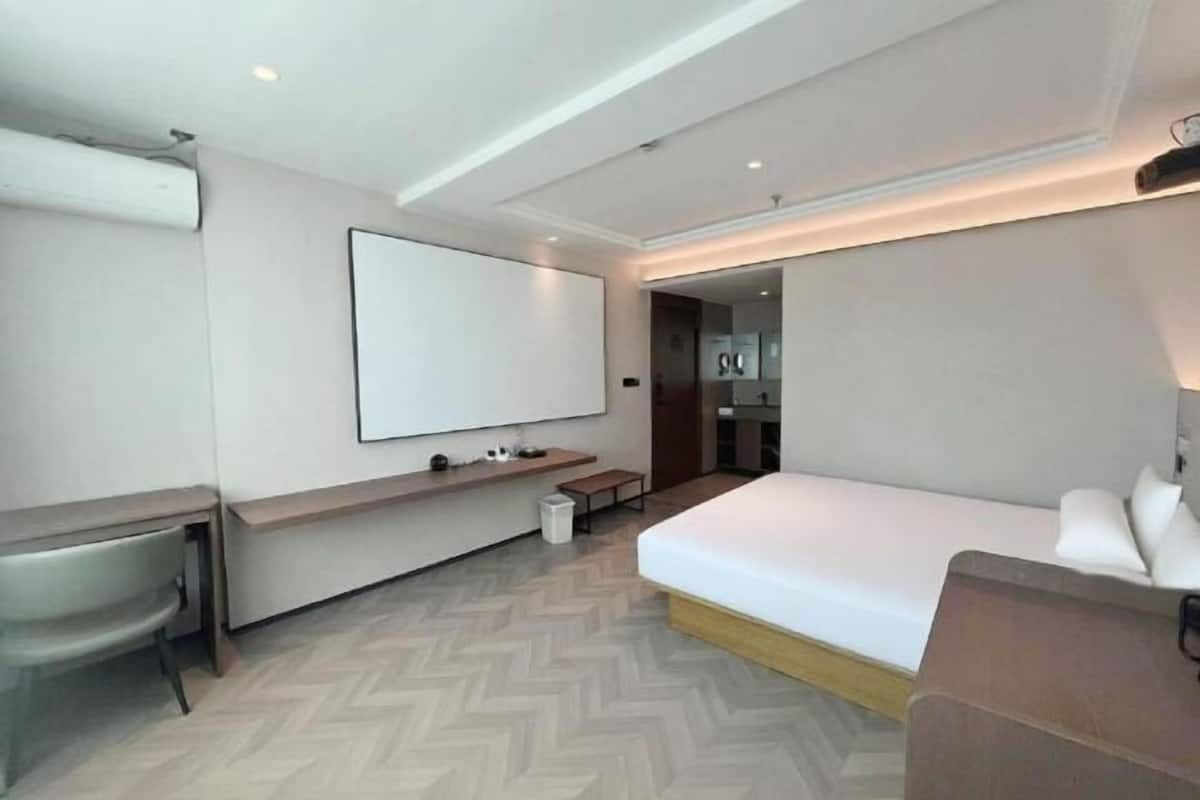 Ein modernes Hotelzimmer mit einem Bett, einem Schreibtisch, einem Sessel, einem Fernseher und einer kleinen Bank.