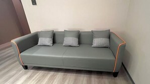 A grey sofa with checkered pillows against a plain wall, in a room with wooden flooring. - Haocheng Business Hotel Ruian City (Rui'an)