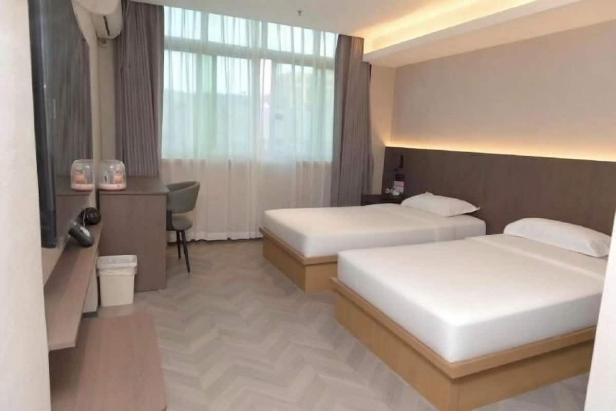 Ein Hotelzimmer mit zwei Betten, einem Schreibtisch, einem Stuhl und einem großen Fenster mit Vorhängen.