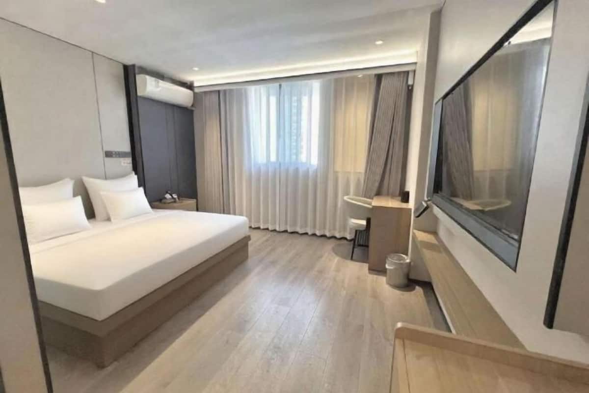 Ein modernes Hotelzimmer mit einem großen Bett, einem Schreibtisch und einem großen Fenster mit Vorhängen.