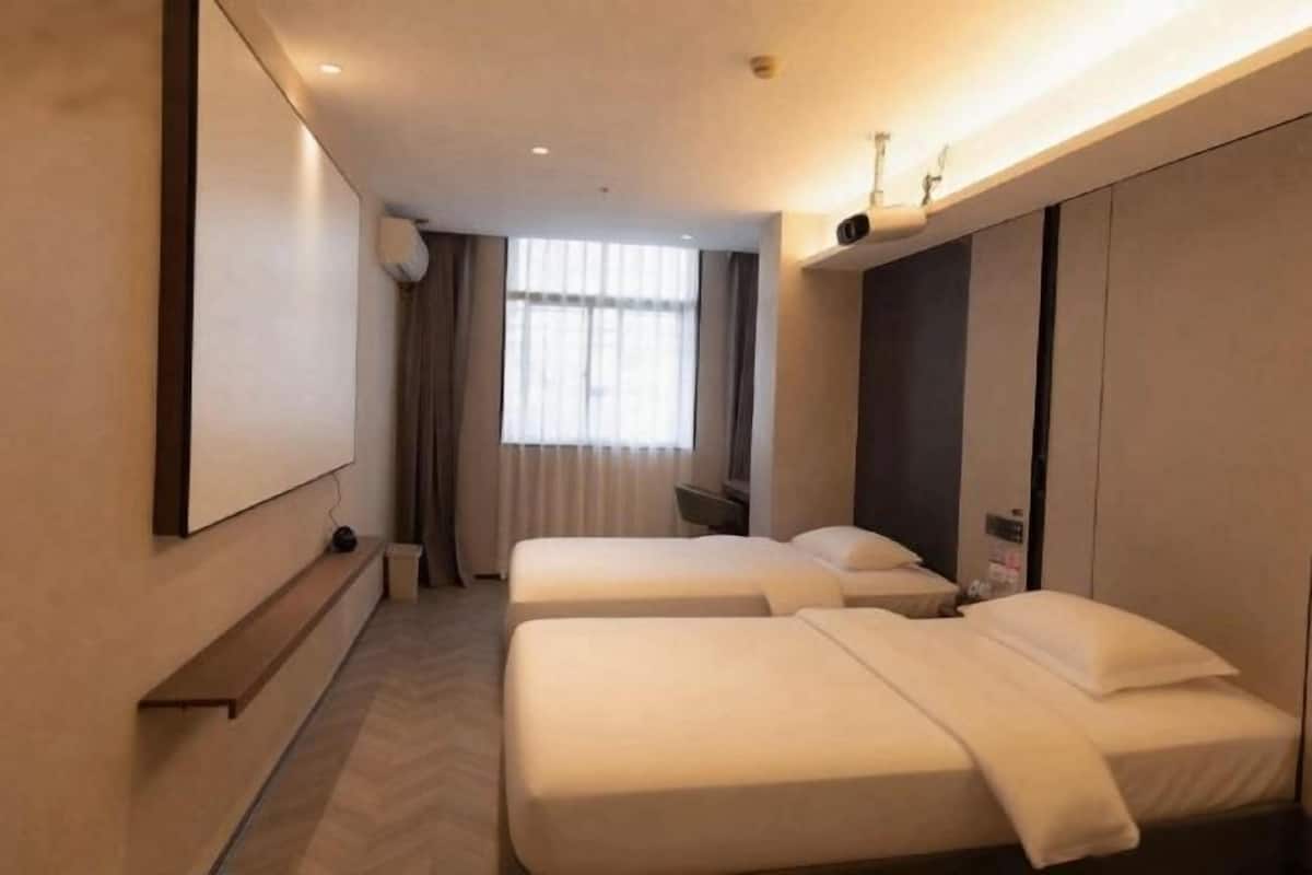Ein Hotelzimmer mit zwei Betten, einem an der Wand montierten Flachbildfernseher, einem Fenster mit Vorhängen und einem Einbauschrank.