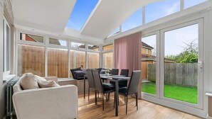 A sunlit room with a dining table, chairs, a sofa, and a sliding glass door leading to a backyard.