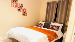 A neatly made bed with a white and orange bedspread, geometric patterned pillows, and a brown headboard.