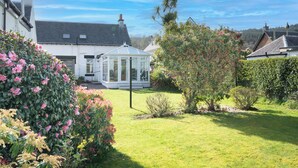 Ein Haus mit Wintergarten, einem gepflegten Garten und blauem Himmel.