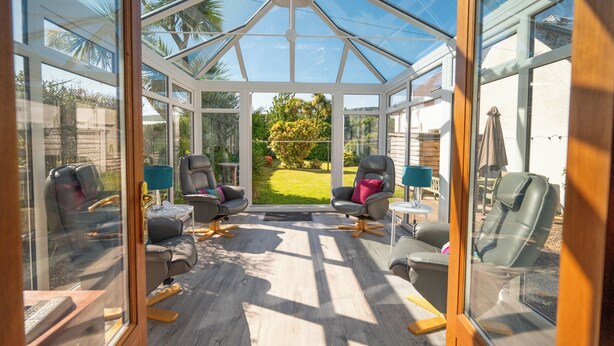 Ein Wintergarten mit Glasdach, zwei Stühle, ein kleiner Tisch und Blick auf einen Garten.