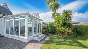 Ein Wintergarten mit Glasdach, umgeben von einem gepflegten Garten mit einer Palme und einer Hecke.